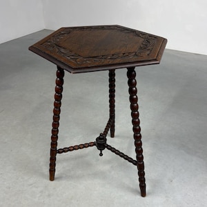 Könnte beinhalten: Ein dunkelbrauner, sechseckiger Beistelltisch mit geschnitztem Blumenrand. Der Tisch hat gedrechselte Beine und eine zentrale Stütze. Der Tisch ist etwa 71 cm hoch.