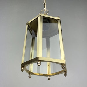Op de afbeelding: Een hanglamp van messing en glas met een zeshoekige vorm en een heldere glazen kap. De lamp hangt aan een ketting.