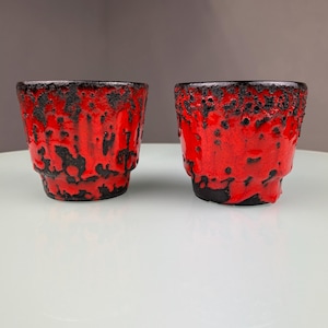 Op de afbeelding: Twee rode en zwarte keramische potten met een getextureerd, lava-achtig glazuur.
