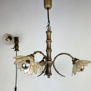 Op de afbeelding: Een kroonluchter met meerdere lampen en een bijpassende wandlamp met een bronskleurig frame in bamboestijl. Elke armatuur is versierd met doorschijnende, bloembladachtige kappen in een bloemvorm, voorzien van zilverkleurige kopspiegellampen.