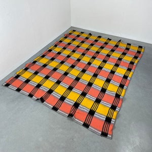 May include: A checkered blanket with black, yellow and pink stripes. The blanket is laid out on a grey concrete floor.