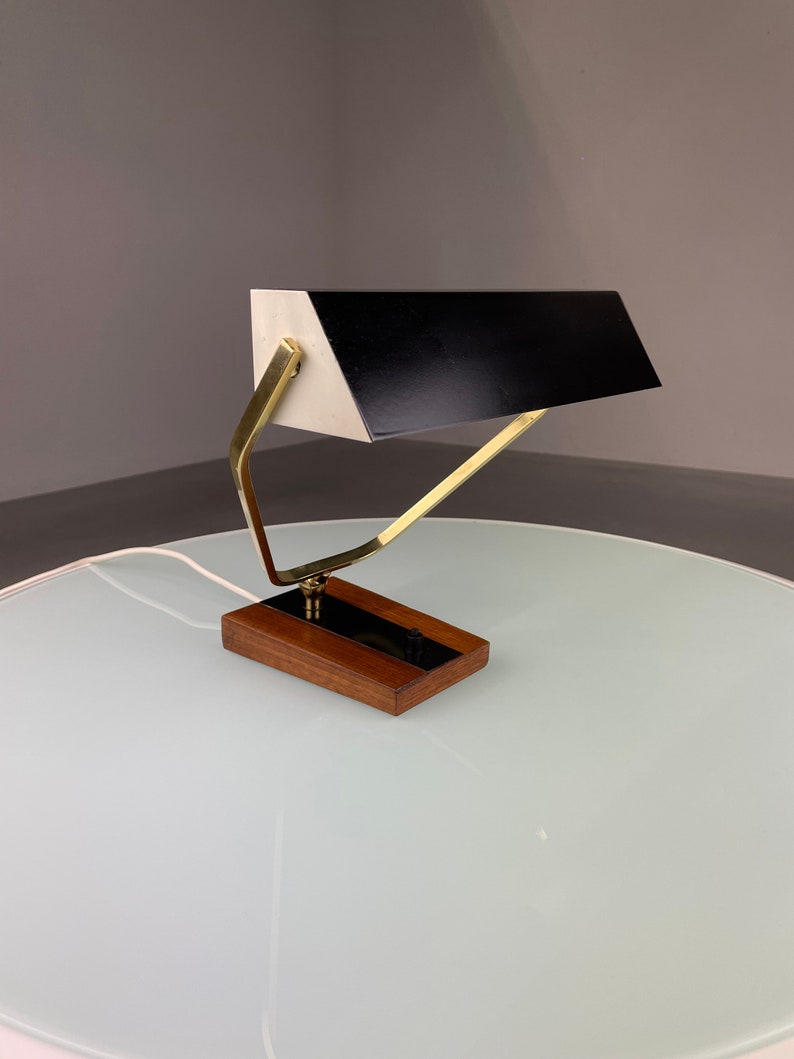 May include: A brass and wood desk lamp with a black and white shade. The lamp has a simple, geometric design and is in good condition.