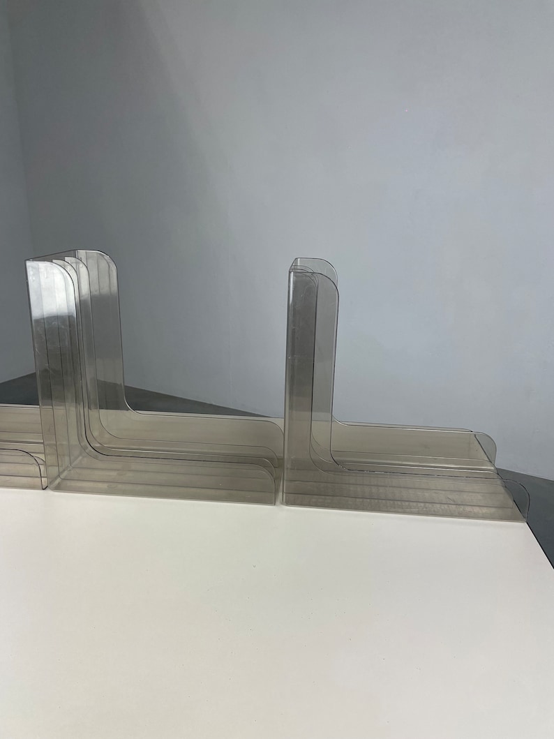 Pu&ograve; includere: Un set di ferma libri in plastica trasparente, impilati e disposti a scalare. I ferma libri sono progettati per tenere i libri in posizione verticale su uno scaffale o una scrivania.