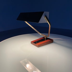 May include: A brass and wood desk lamp with a black shade. The lamp has a simple, geometric design and is in a minimalist style.