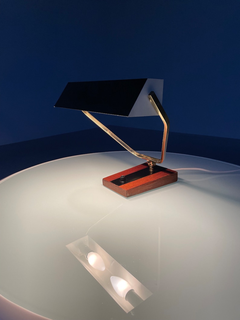 May include: A brass and wood desk lamp with a black shade. The lamp has a simple, geometric design and is in a minimalist style.