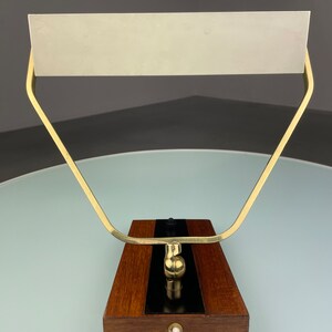 May include: A brass and wood desk lamp with a white shade. The lamp has a simple, geometric design and a black switch on the base.
