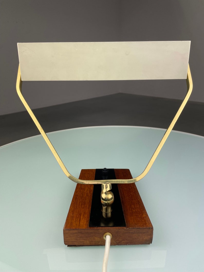 May include: A brass and wood desk lamp with a white shade. The lamp has a simple, geometric design and a black switch on the base.
