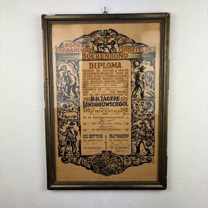 Op de afbeelding: Een antiek ingelijst diploma met Nederlandse tekst en illustraties. Het diploma zit in een donkere houten lijst en bevat zwart-bruine inkttekeningen van mensen, dieren en landbouwscènes. De tekst bevat de woorden "Diploma" en "Boerenbond".