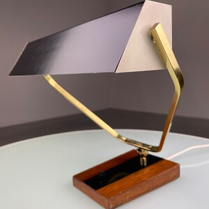 May include: A mid-century modern desk lamp with a brass frame and a black and white metal shade. The lamp has a wooden base and a black switch.