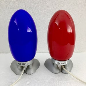 May include: Two egg-shaped lamps with silver bases. The lamp on the left is blue and the lamp on the right is red. Both lamps have a label that reads "MAX 40W".