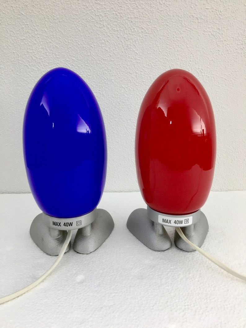 May include: Two egg-shaped lamps with silver bases. The lamp on the left is blue and the lamp on the right is red. Both lamps have a label that reads "MAX 40W".