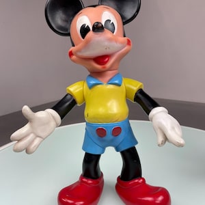 May include: A vintage plastic Mickey Mouse toy with black ears, a yellow shirt, blue shorts, and red shoes.