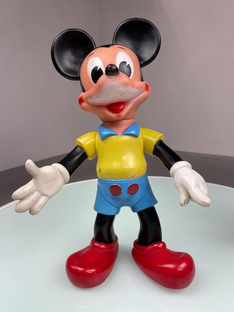 May include: A vintage plastic Mickey Mouse toy with black ears, a yellow shirt, blue shorts, and red shoes.