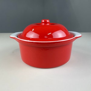 Op de afbeelding: Een rode keramische ovenschaal met een witte rand en een deksel. De schaal heeft een glanzende afwerking.