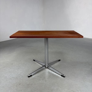 May include: A rectangular wooden table with a rich brown finish. It has a single, polished chrome leg that extends to a four-point base. The table is approximately 76 cm long and 51 cm wide.