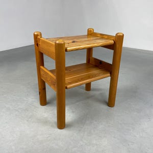 Op de afbeelding: Een houten bijzettafel met twee niveaus en een natuurlijke afwerking. De tafel heeft een rechthoekig blad en een onderste plank, ondersteund door vier afgeronde poten. De tafel is ongeveer 61 cm hoog en 46 cm breed.