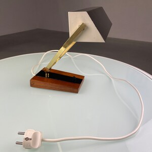 May include: A black and white desk lamp with a brass arm and a wooden base. The lamp has a white cord and a two-prong plug.