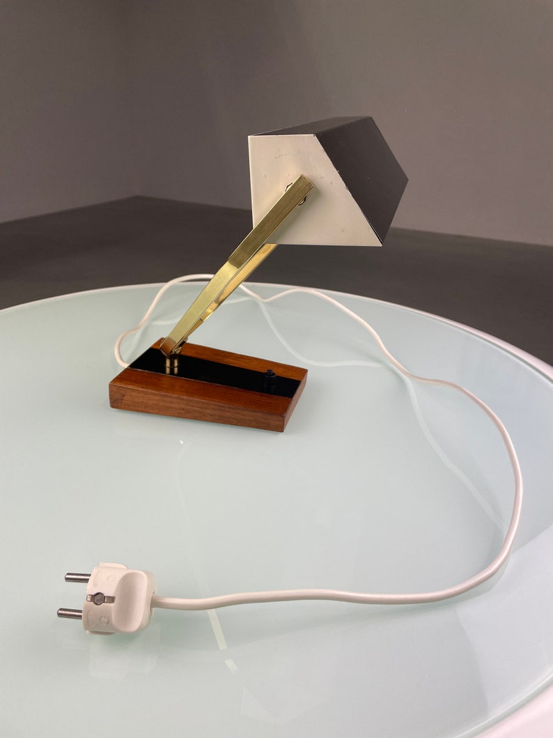 May include: A black and white desk lamp with a brass arm and a wooden base. The lamp has a white cord and a two-prong plug.