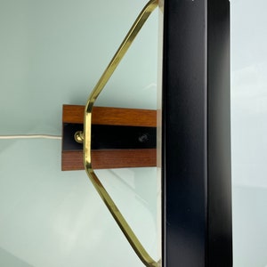 May include: A black and brass wall mounted lamp with a rectangular shade. The lamp has a wooden base with a brass arm.