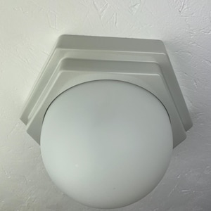 Op de afbeelding: Een witte plafondlamp met een ronde, matte glazen kap.