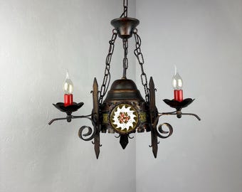 May include: An antique chandelier with a dark bronze finish. It features two candle-style lights with red bases and decorative scrollwork. A central panel displays a floral design.