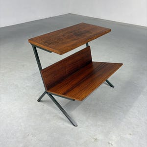 May include: A mid-century modern side table with a dark wood top and shelf. The table has a unique angled design with a dark metal frame. The wood has a rich, warm tone, and the table is set against a neutral background.