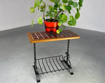 Puede incluir: Una pequeña mesa auxiliar de metal negro con una tapa de azulejos y un estante inferior. Una planta en maceta con hojas redondas y verdes se encuentra sobre la mesa. La maceta es roja y negra.