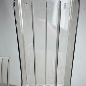 Pu&ograve; includere: Porta riviste in plastica trasparente con quattro scomparti verticali. Il porta riviste ha una base curva e due fori nella parte superiore.