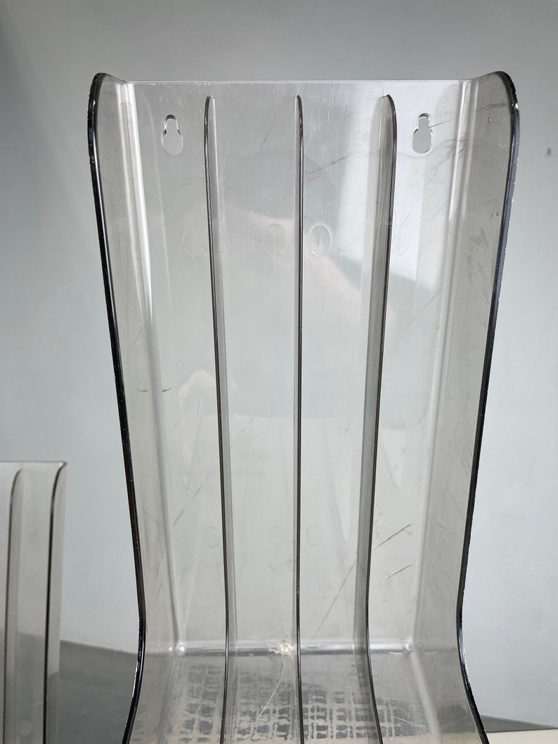 Pu&ograve; includere: Porta riviste in plastica trasparente con quattro scomparti verticali. Il porta riviste ha una base curva e due fori nella parte superiore.