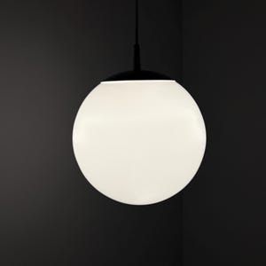 Op de afbeelding: Een moderne hanglamp met een grote, bolvormige, witte glazen kap. De kap hangt aan een zwart armatuur en snoer tegen een donkere achtergrond. Het ontwerp is minimalistisch en eigentijds.