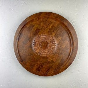 Op de afbeelding: Een ronde houten serveerschaal met een geruit patroon en een gegraveerd stervormig ontwerp in het midden.