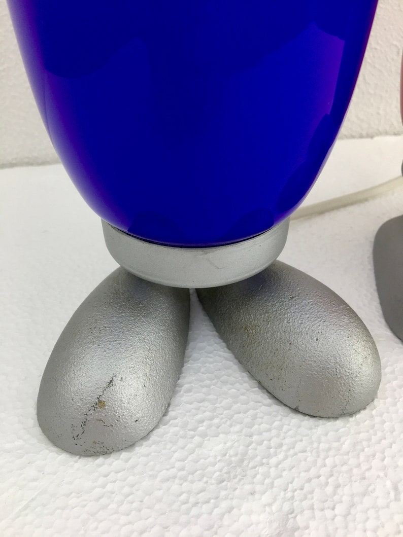 May include: A pair of blue and pink glass lamps with silver bases and feet. The lamps are shaped like a rounded rectangle and have a smooth, glossy finish.