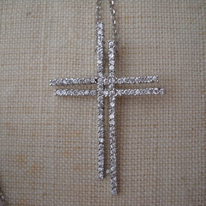 Pode incluir: Um colar de prata com um pingente de cruz cravejado de diamantes. A cruz &eacute; feita de duas barras sobrepostas, cada uma cravejada com pequenos diamantes.