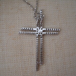 Pode incluir: Colar com pingente de cruz em tom prateado com uma dupla fileira de pedras transparentes. O pingente est&aacute; preso a uma corrente em tom prateado.