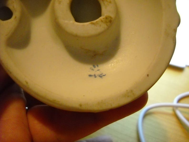May include: Close-up of the bottom of a white porcelain figurine. The bottom has a blue mark with the letters "D-E" inside.