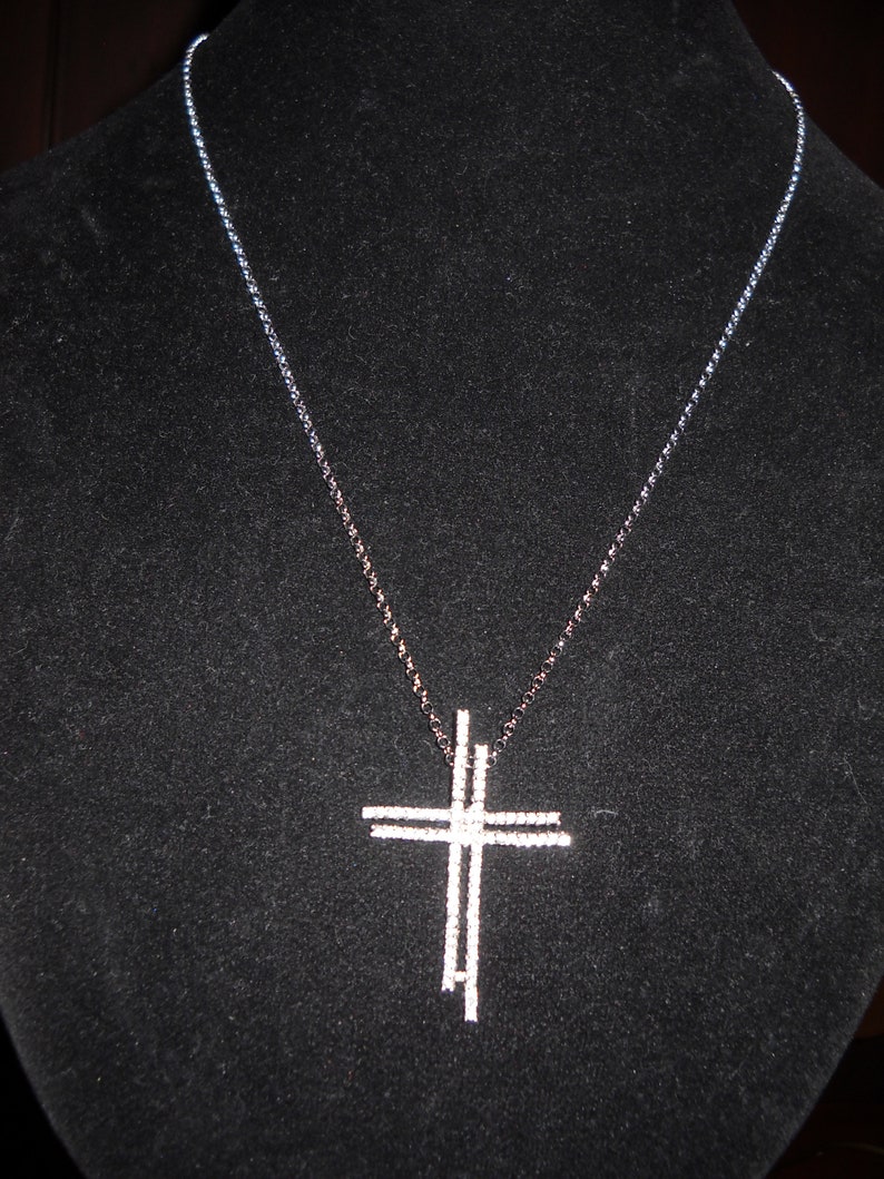 Pode incluir: Um colar de prata com um delicado pingente de cruz de v&aacute;rias camadas. A corrente &eacute; de prata e tem uma textura de corda.