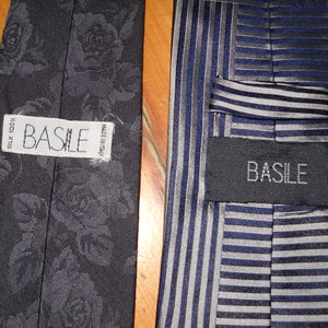 May include: Two black silk ties with the brand name "BASILE" printed on the label. One tie has a floral pattern and the other has a striped pattern.