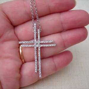 Pode incluir: Um colar de corrente de prata com um grande pingente de cruz de prata incrustado com pedras de zirc&ocirc;nia c&uacute;bica transparentes.