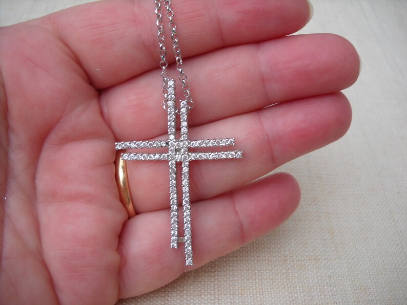 Pode incluir: Um colar de corrente de prata com um grande pingente de cruz de prata incrustado com pedras de zirc&ocirc;nia c&uacute;bica transparentes.