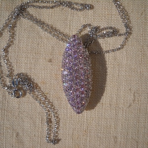 May include: A silver chain necklace with a large oval pendant covered in pink and clear rhinestones.