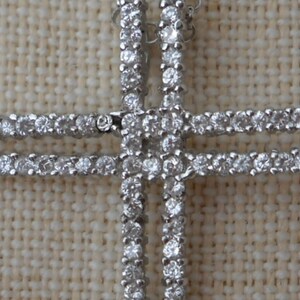 Pode incluir: Um pingente de cruz de prata com uma dupla fileira de pedras de zirc&ocirc;nia c&uacute;bica transparentes.