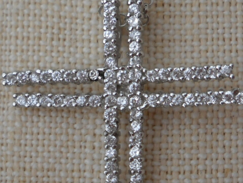 Pode incluir: Um pingente de cruz de prata com uma dupla fileira de pedras de zirc&ocirc;nia c&uacute;bica transparentes.