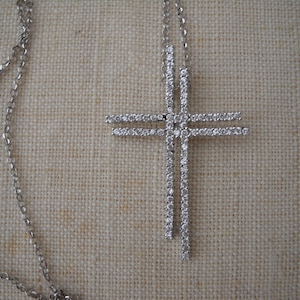 Pode incluir: Um colar de corrente de prata com um grande pingente de cruz cravejado de diamantes.