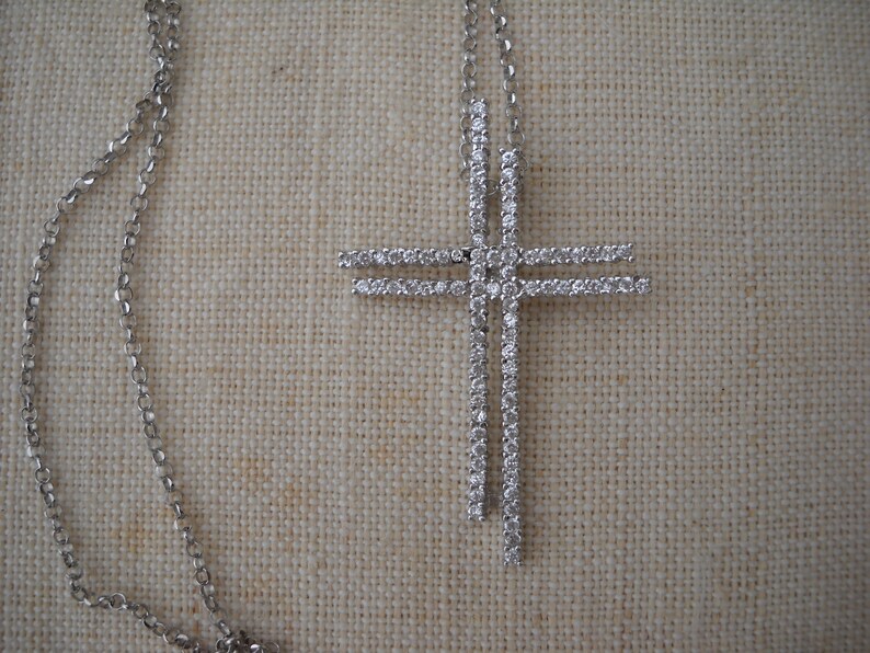 Pode incluir: Um colar de corrente de prata com um grande pingente de cruz cravejado de diamantes.