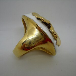 May include: A gold ring with a white enamel design. The ring has a unique, abstract shape.