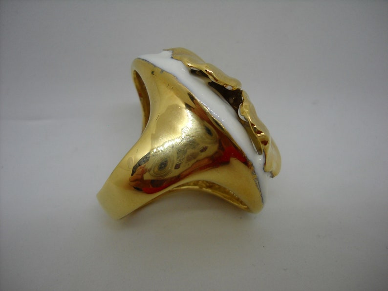 May include: A gold ring with a white enamel design. The ring has a unique, abstract shape.