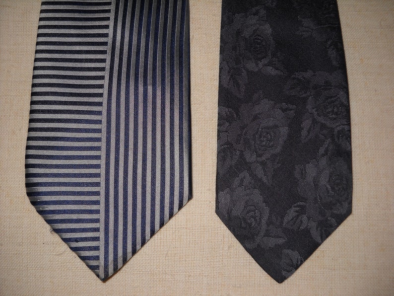 May include: Two neckties, one with a striped pattern in shades of grey and blue, and the other with a black background and a floral pattern of grey roses.