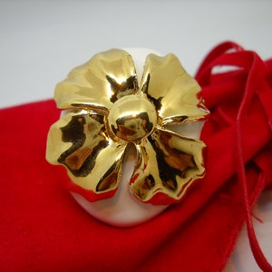 May include: A white ceramic egg with a gold flower design. The egg is sitting on a red velvet bag.