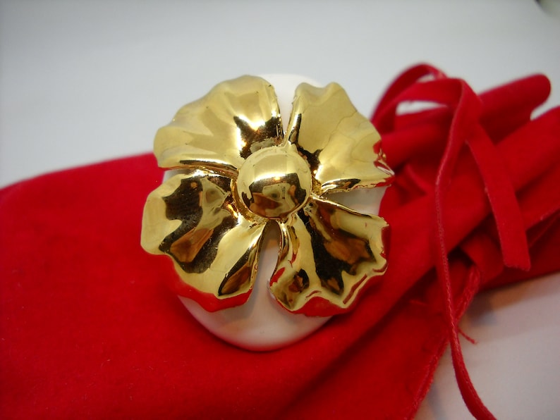 May include: A white ceramic egg with a gold flower design. The egg is sitting on a red velvet bag.