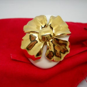 May include: A white ceramic flower with gold accents. The flower is shaped like a bow and has a center with a raised, round, gold detail.